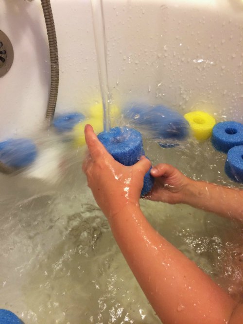 child playing with pool noddles in tub