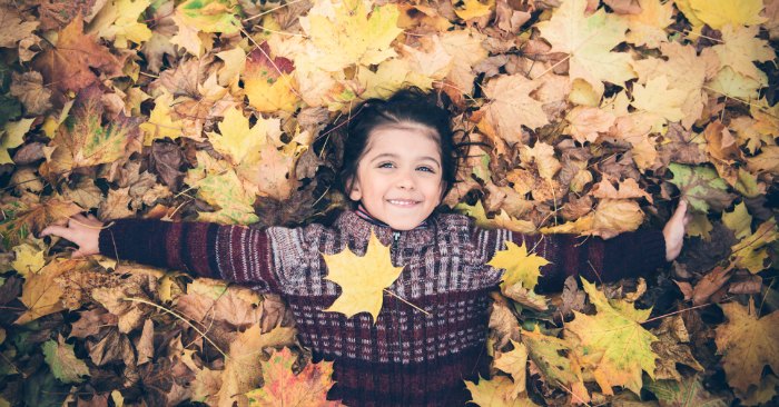 young girl laying in pile of leaves