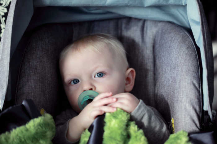 baby in car seat carrier with green pacifier