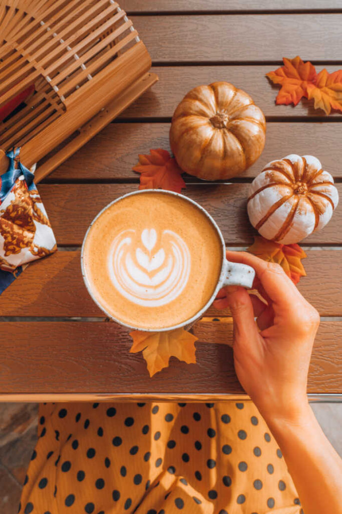 women holding pumpkin spice latte with pumpkins on table