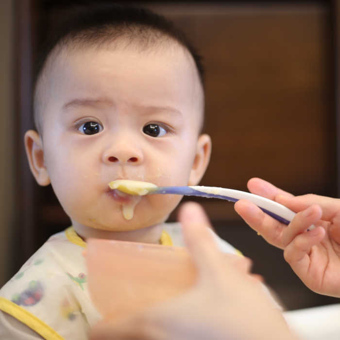 Baby with funny expression being spoon fed solid food