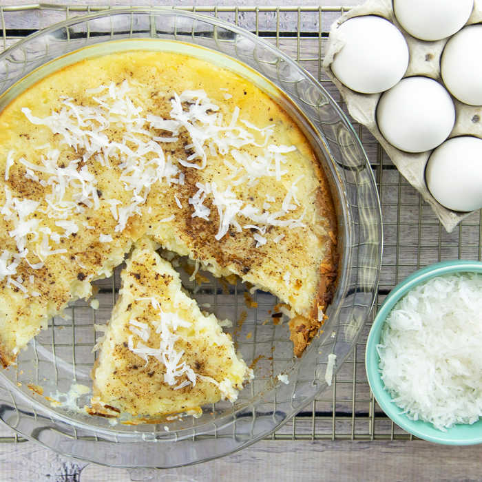 coconut custard pie slice with rest of pie, eggs and coconut on the side