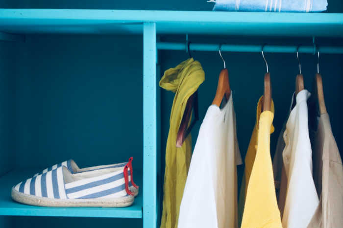 bright blue interior of closet with several clothes hanging and a shelf for shoes
