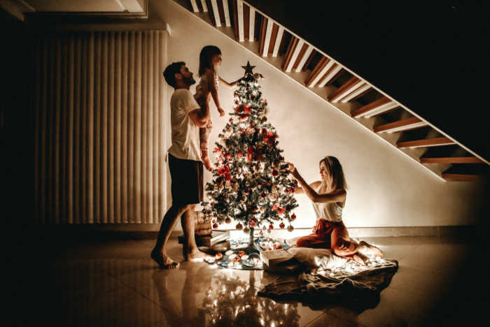 mom and dad decorating tree lit up with little girl