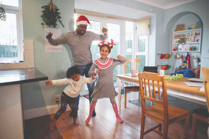 Family of dad and 2 daughters dancing stress free in Christmas pajamas in the kitchen
