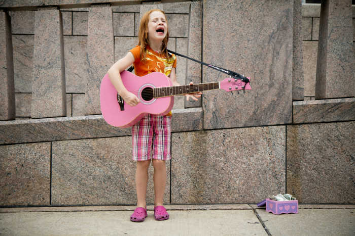 girl singing playing guitar to earn money