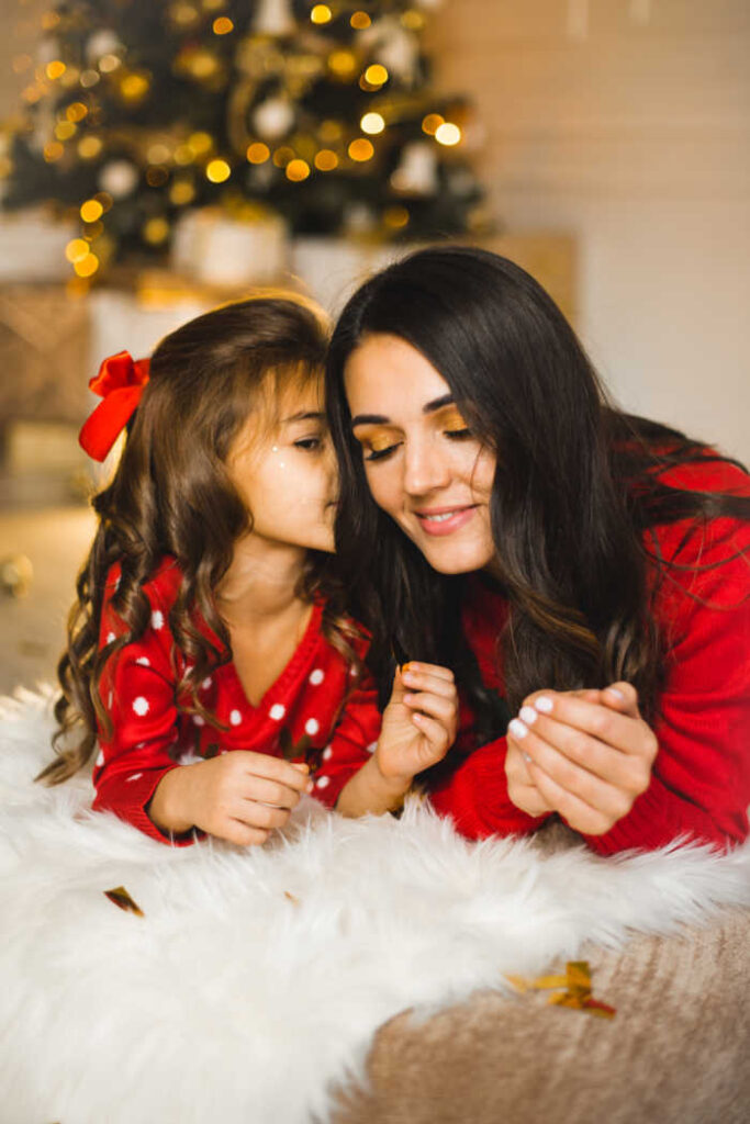 girl whispering to mom with christmas tree in background