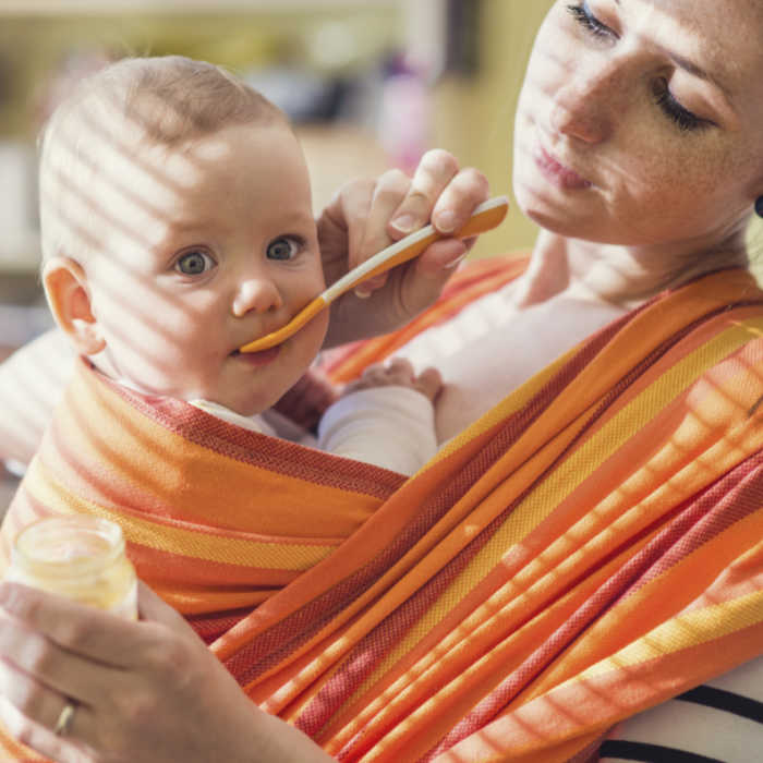 Baby strapped to mom being spoon fed