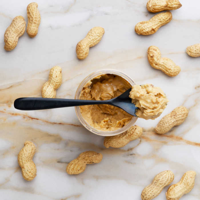 chunky peanut butter on a spoon surrounded by unshelled peanuts