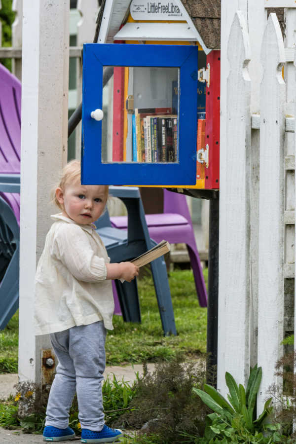toddler holding a book from a free little library stand