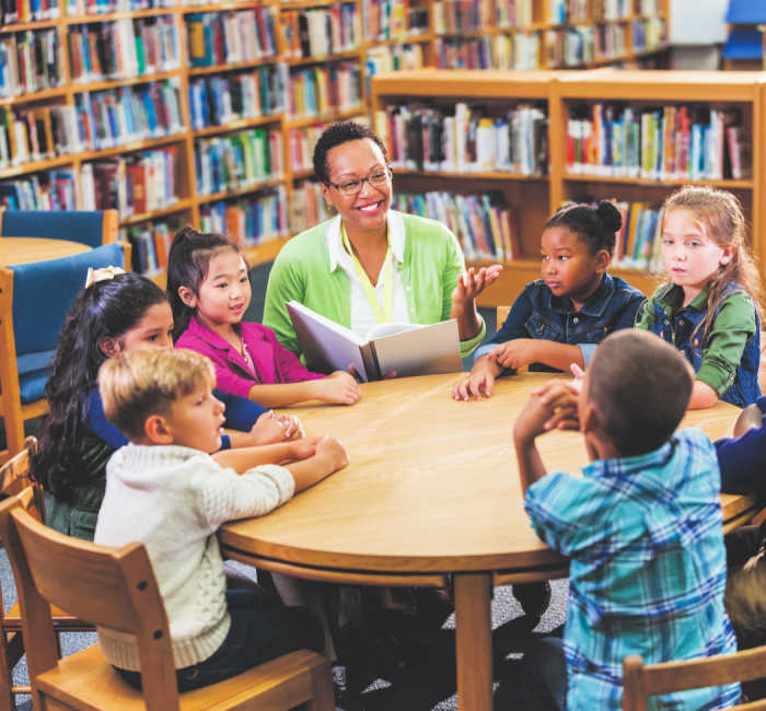 librarian reading with elementary children around table at the library