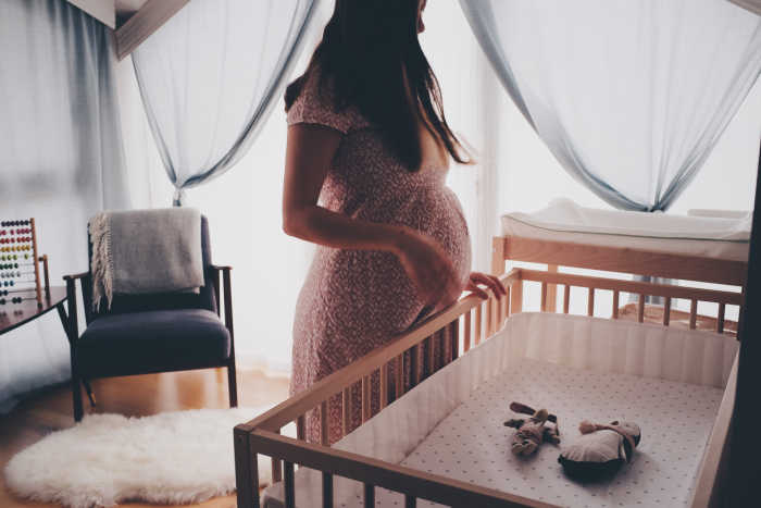 pregnant woman standing in front of crib in baby nursery