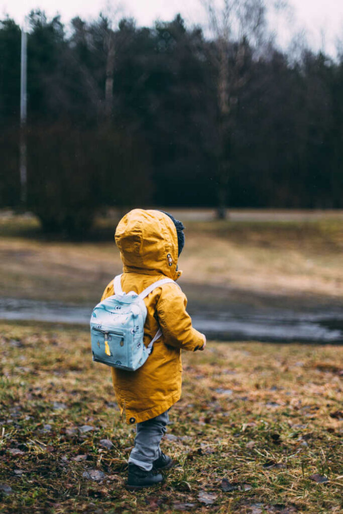 preschoolers walking in rain with yellow rain jacket and small backpack