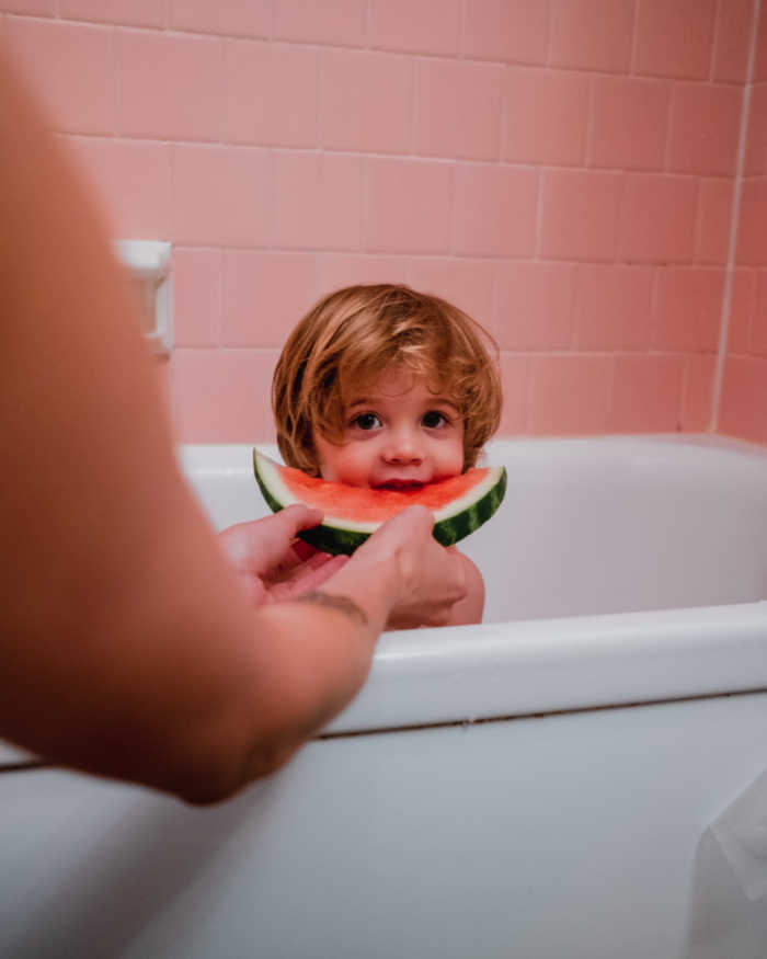 child eating watermelon in bath tub before washing toddlers hair