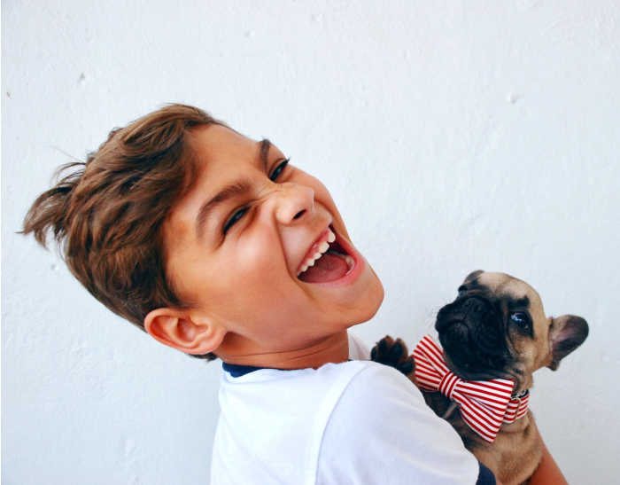 middle school boy laughing holding pug dog with red and white striped bowtie on