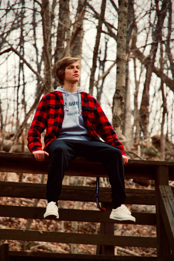 teenage boy in red checked shirt sitting on wooden fence during the fall season
