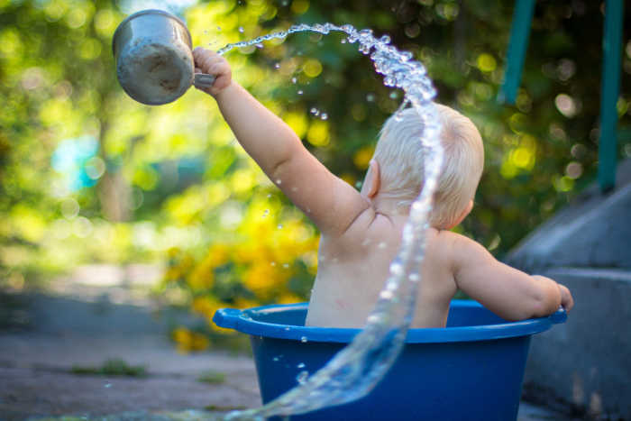 child throwing water from cup while sitting in tub outside