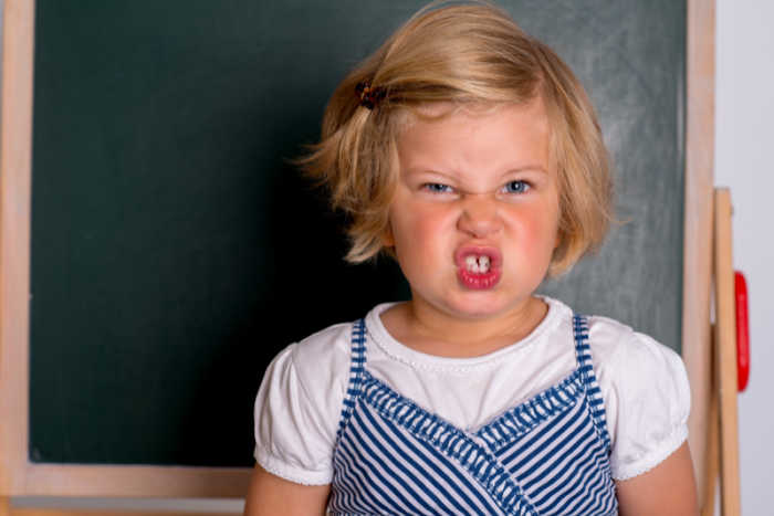 elementary age blonde girl with face scrunched up in anger in front of chalk board