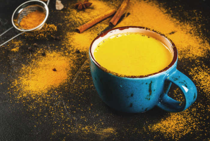 Traditional Indian drink turmeric milk is golden milk with cinnamon, cloves, pepper and turmeric. On a concrete table, with spices on the background. In a large cup.