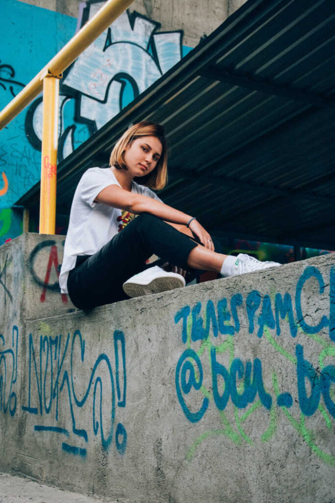 teenage girl in urban area sitting on concrete ledge with graffiti