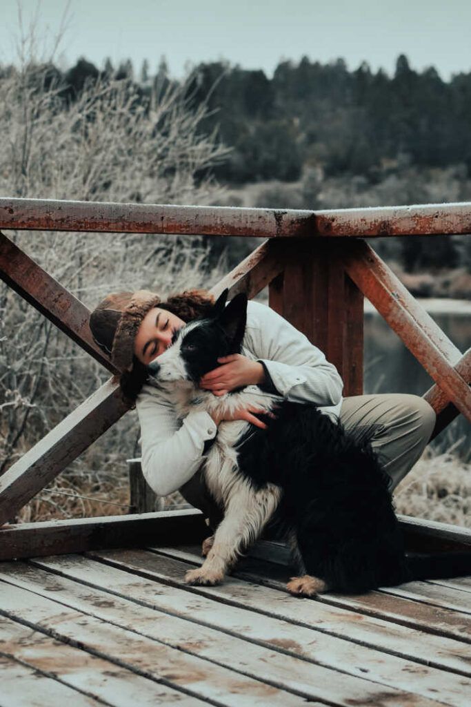 girl hugging border collie black and white dog in wintertime on deck - shows the benefits of owning a pet