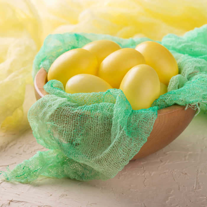 Yellow Eater Eggs on green linen cloth in wood bowl
