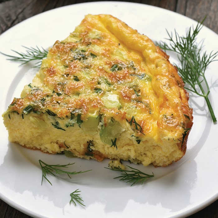 Slice of herbed spanish omelet on white plate with spring herbs