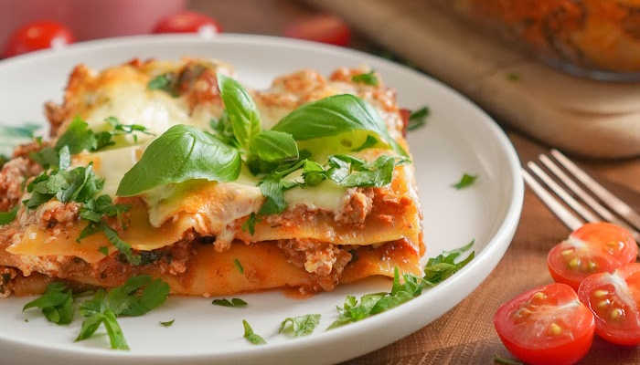 piece of homemade lasagna on white plate with sprig of basil