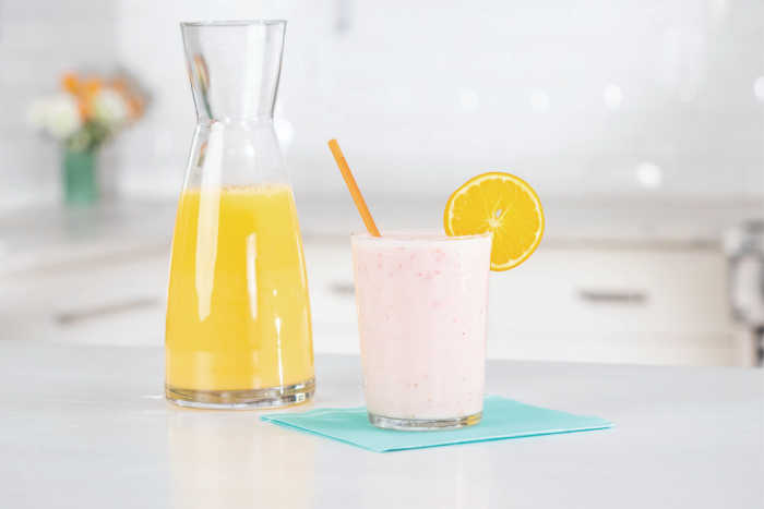 caraffe of orange juice next to glass of berry smoothie with slice of orange on glass