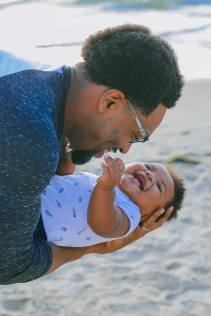 black father laughing playing with infant at beach