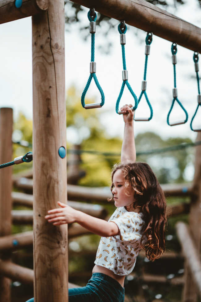 young girl swinging on monkey rings at playground