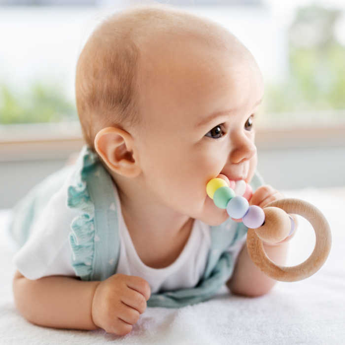 teething infant chewing on wooden ring