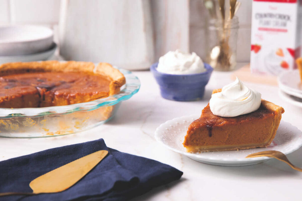 slice of pumpkin on white plate, full pie in background with pie knife