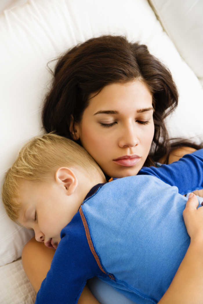 Caucasian mid adult woman with toddler son hugging and sleeping in bed.