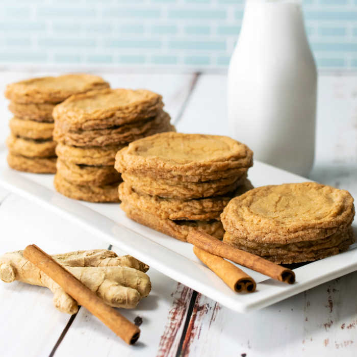 Ginger cookies on a white plate with cinnamon sticks and fresh ginger