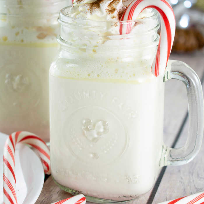 White hot chocolate in fun mugs with a candy cane and topped with cinnamon