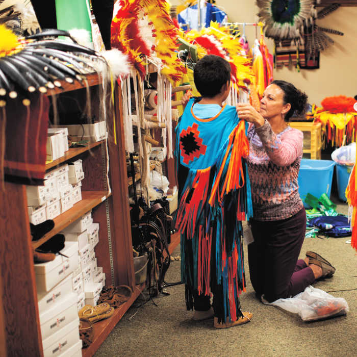 woman dressing child in traditional feathers to reinforce cultural heritage and identity