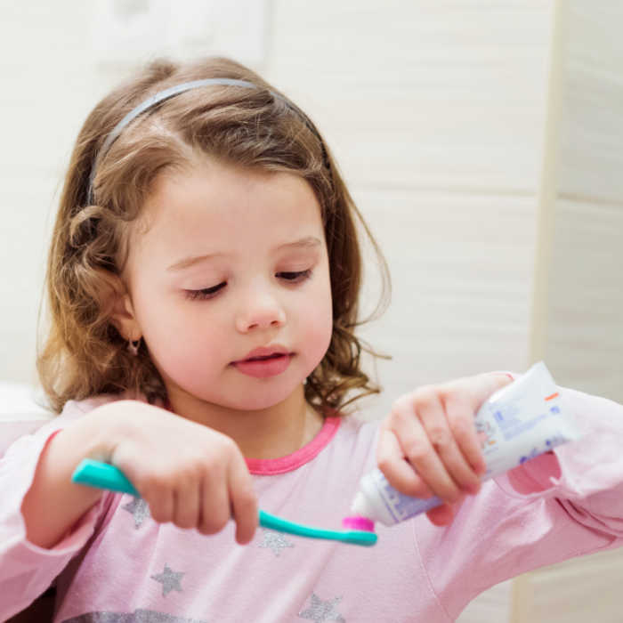 cute little girl in pink pajamas putting pink toothpaste on her toothbrush