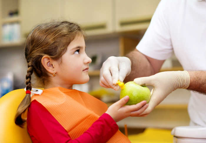 dentist showing young girl how to brush using a green apple