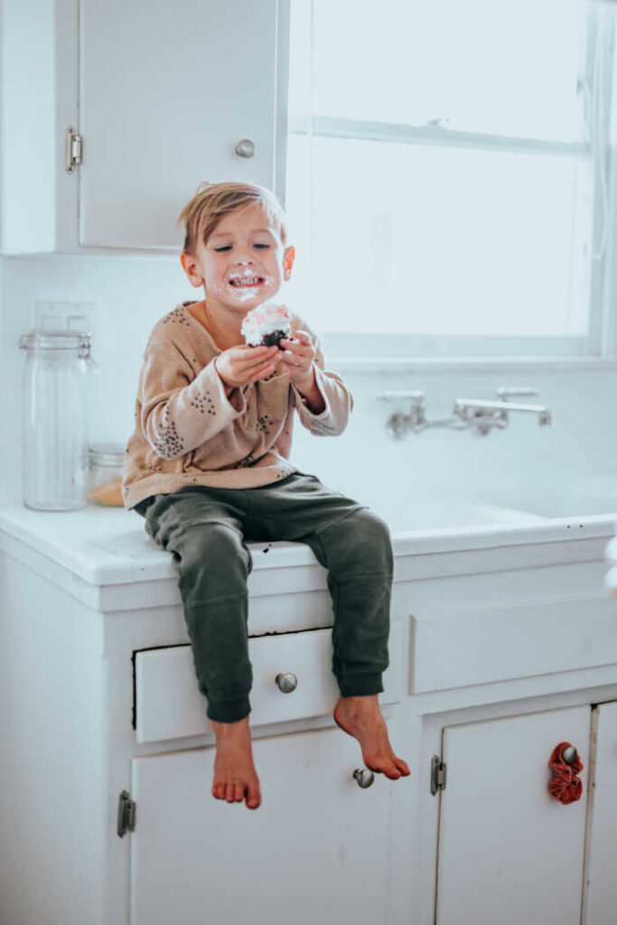 messy kid eating donut sitting on kitchen counter