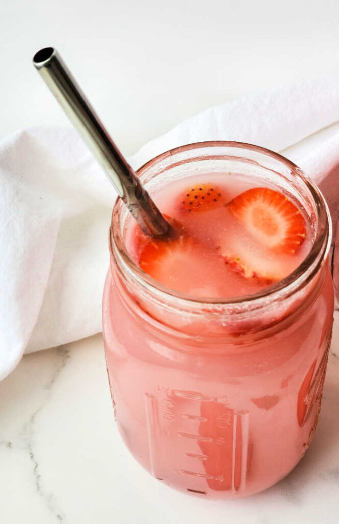 pink drink with strawberries floating with metal straw in glass jar