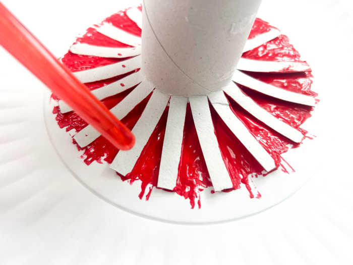 Step for firework craft - Dip the toilet paper roll into the paint. To make sure all of the strips are covered, use the end of a paintbrush to gently press down into the paint. Continue this step until the strips are evenly covered. 