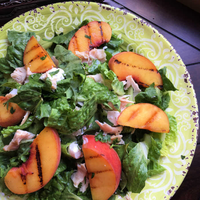 grilled peaches salad on a fun green plate with chicken pecans and goat cheese