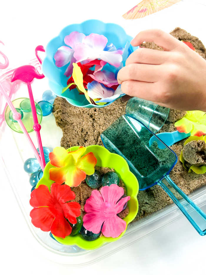 having fun with tropical summer sensory bin - including scoops, lei flowers and sand