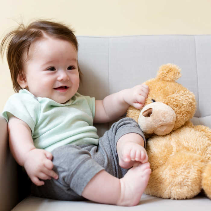 baby boy sitting with stuffed teddy bear on couch