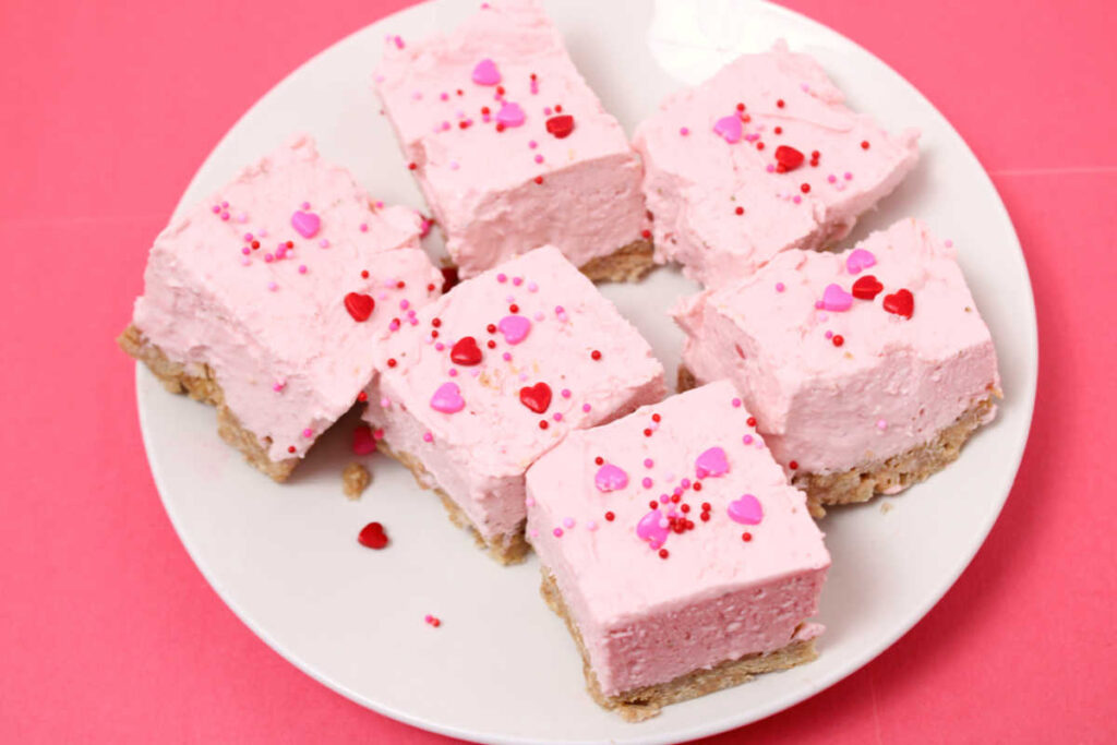 no bake strawberry cheesecake bars on a plate with pink background