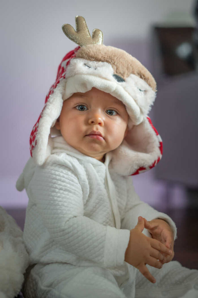 baby in white outfit wearing christmas reindeer hat