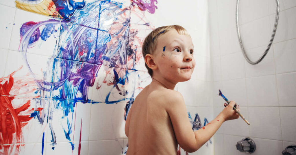 young boy painting shower bath walls with paint brush 