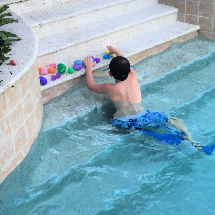 boy wearing swim fins counting his eggs after a fun easter egg hunt in the pool