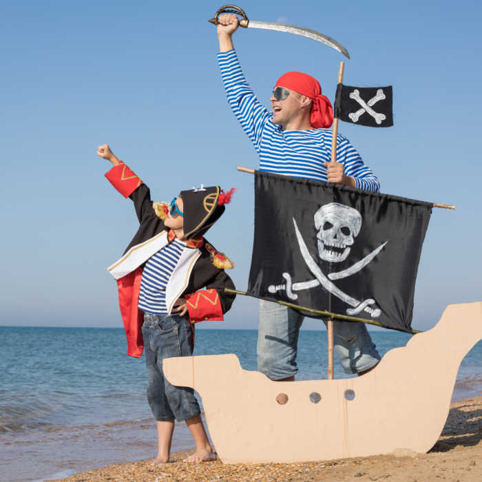 Father and son playing on the beach at the day time. They are dressed in sailor's vests and pirate costumes. Concept of happy game on vacation and friendly family.